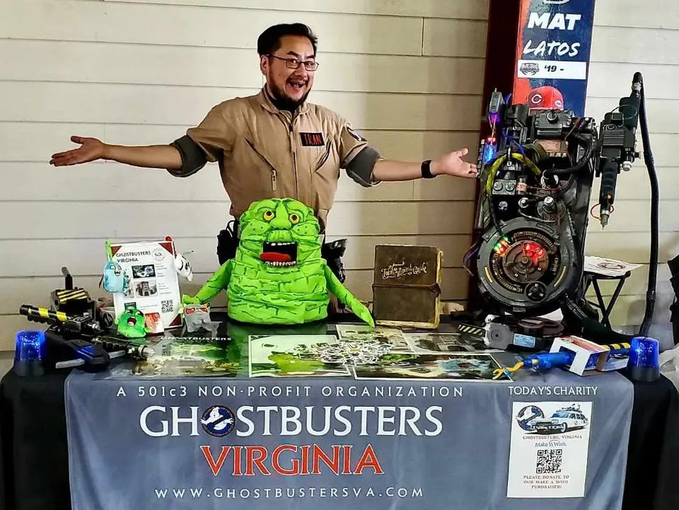 Ghostbusters Virginia member sitting at an event table with a Slimer prop